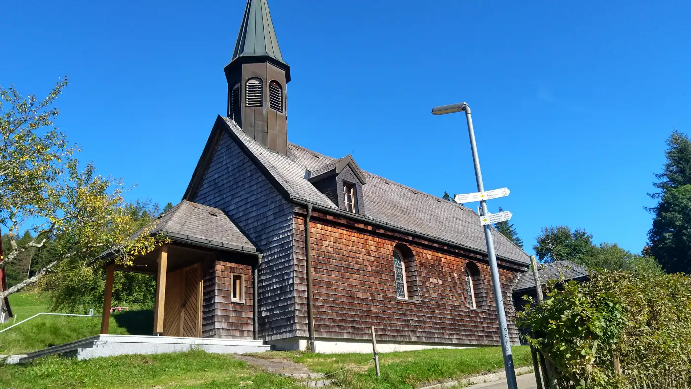 Bildtitel: Hölzerne Wendelinkapelle in Linach unter strahlend blauem Himmel